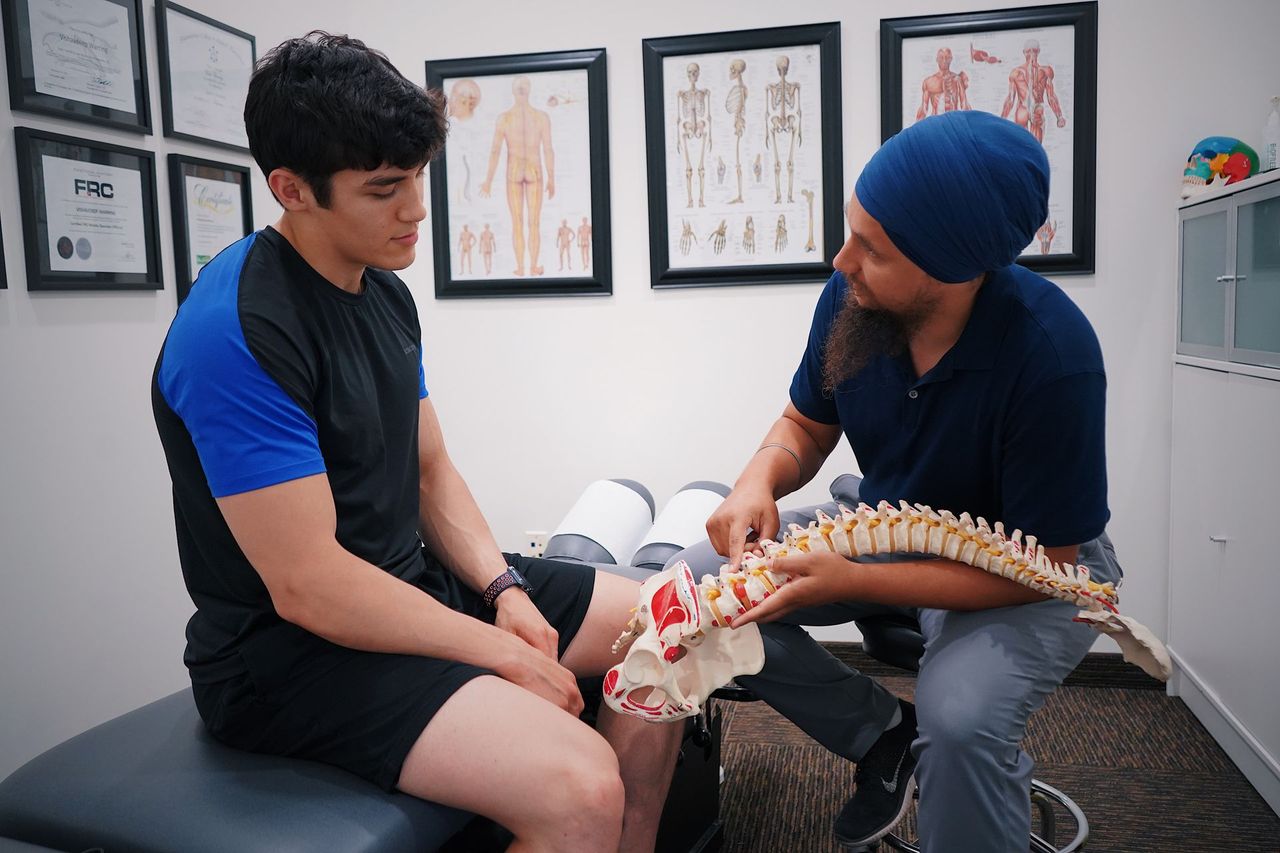 A chiropractor explaining spinal anatomy to a patient using a model of the spine